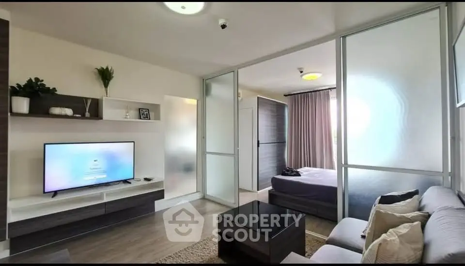 Modern living room with sleek furniture and TV, adjacent to a cozy bedroom.