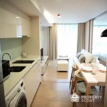 Modern studio apartment with integrated living space, featuring a sleek kitchen with white appliances, a cozy dining area, and a comfortable seating zone bathed in natural light from the large window.