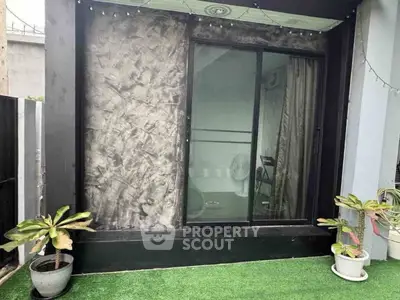 Modern balcony with artificial grass and potted plants, featuring sliding glass doors.