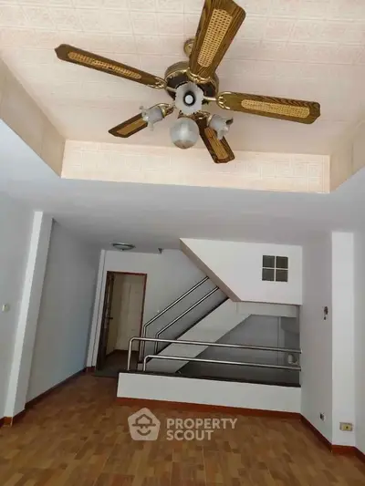 Spacious interior with ceiling fan and staircase, featuring elegant wooden flooring.