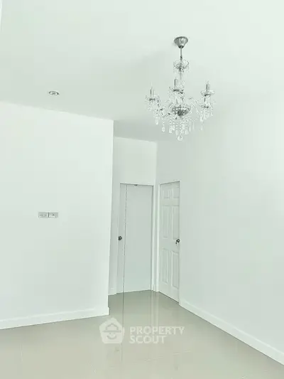 Spacious white room with elegant chandelier and glossy tiled floor, perfect for modern living.
