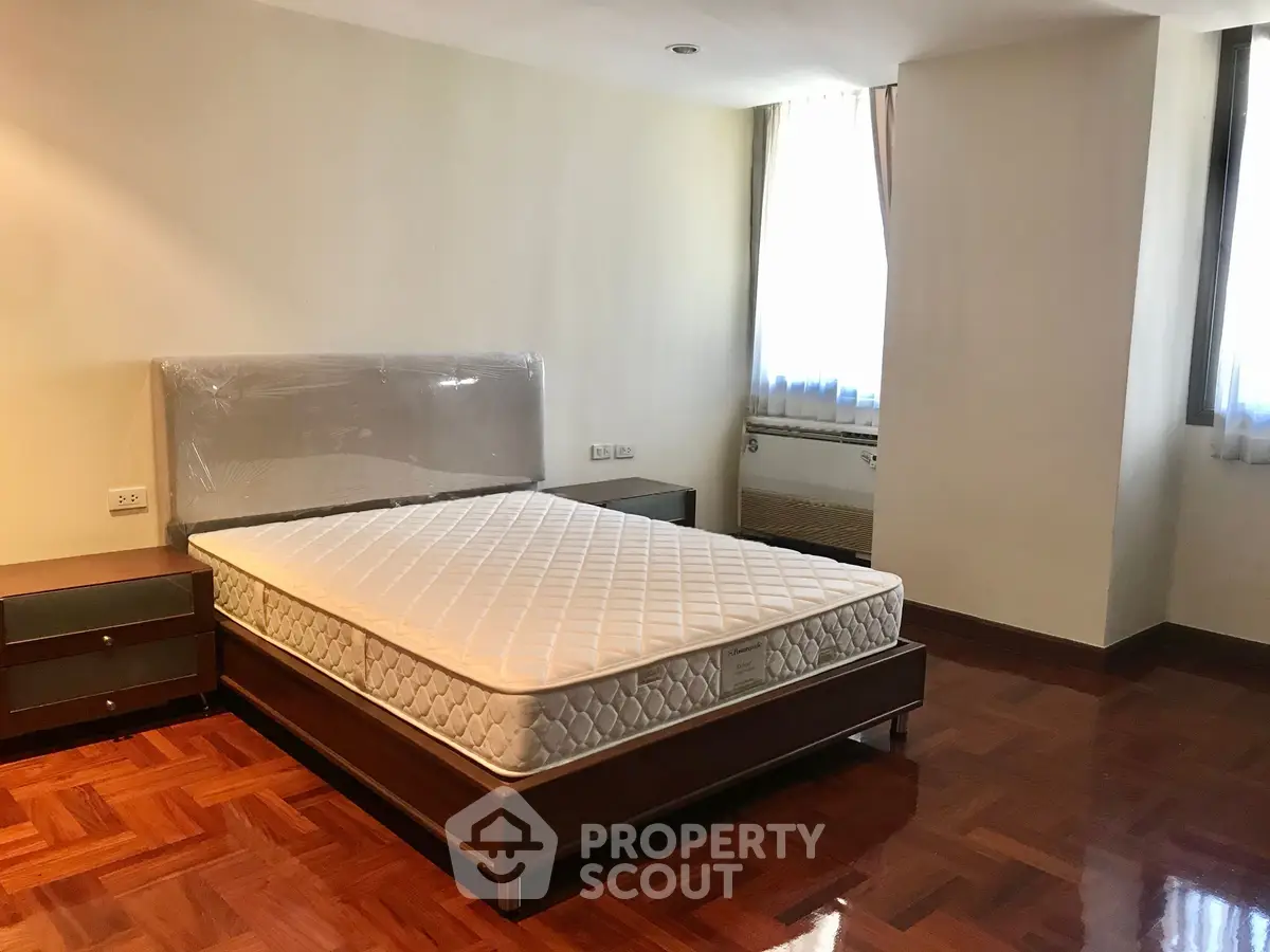 Spacious bedroom with parquet flooring and natural light, featuring a modern bed and side tables.