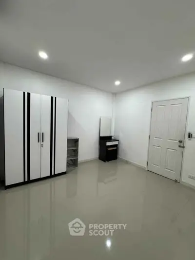 Spacious minimalist bedroom with sleek wardrobe and modern vanity in a bright, white interior.