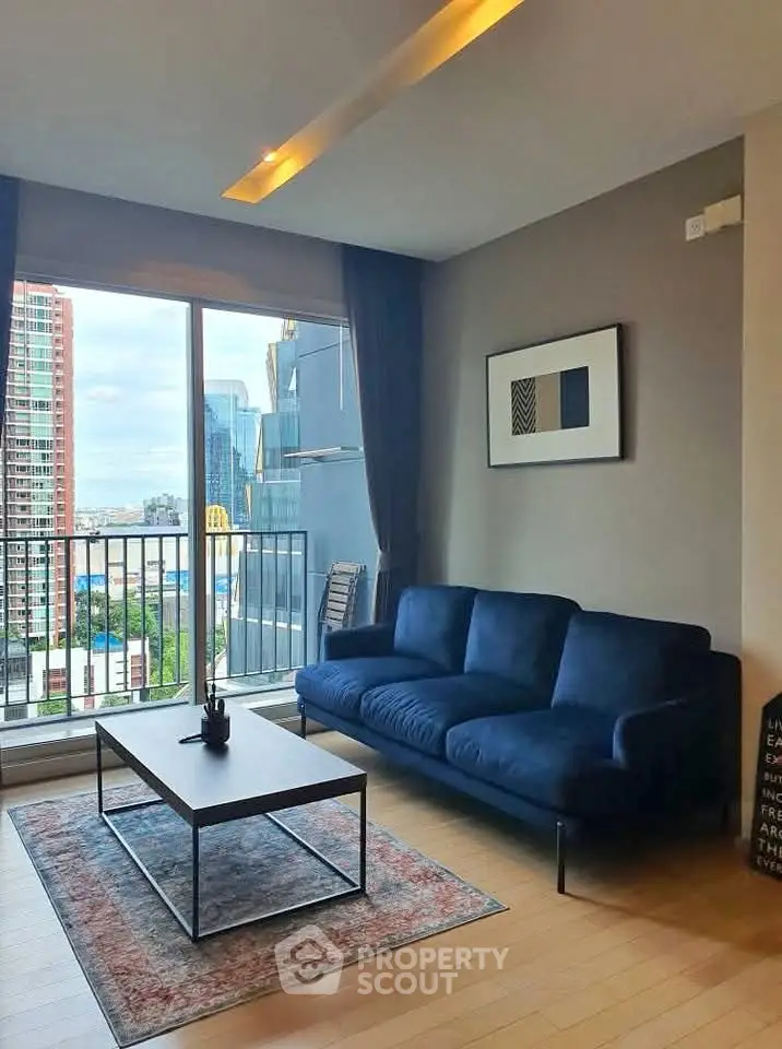 Modern living room with blue sofa and city view from balcony, featuring stylish decor and natural light.
