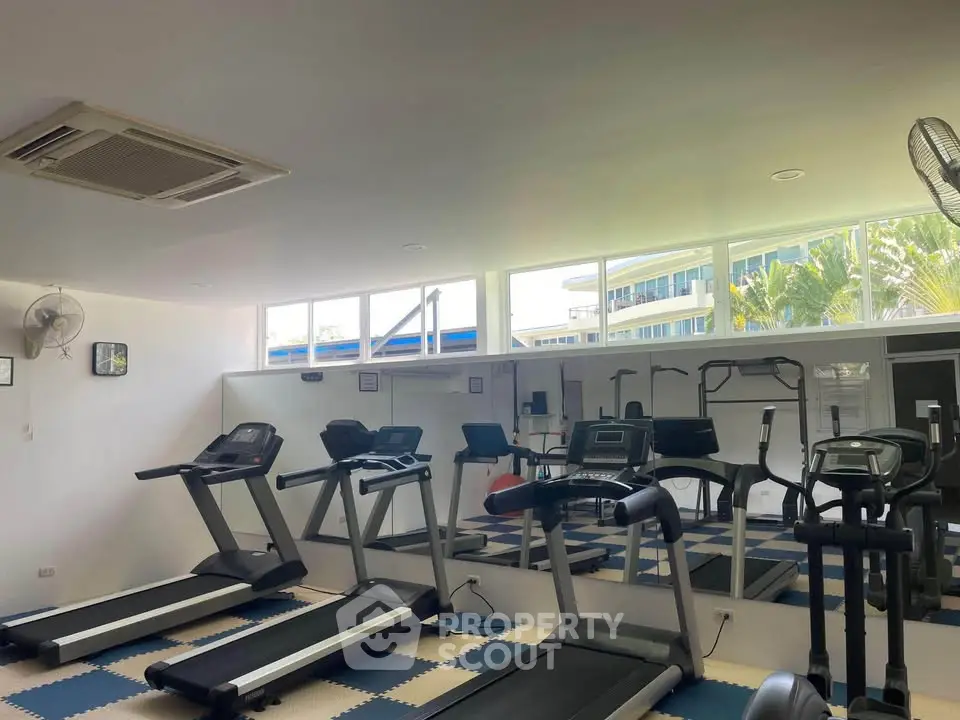 Modern gym with treadmills and exercise equipment in a bright, spacious room with large windows.