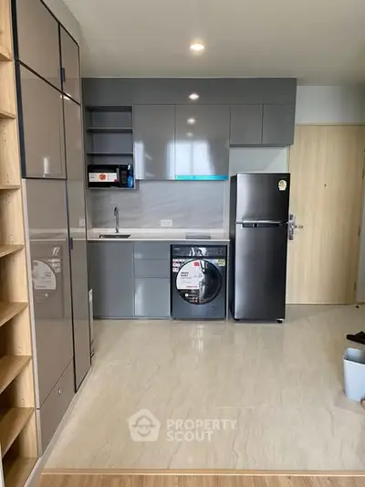 Modern kitchen with sleek cabinets, washing machine, and fridge in a compact layout.