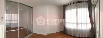 Spacious empty room with wooden flooring and large window with curtains