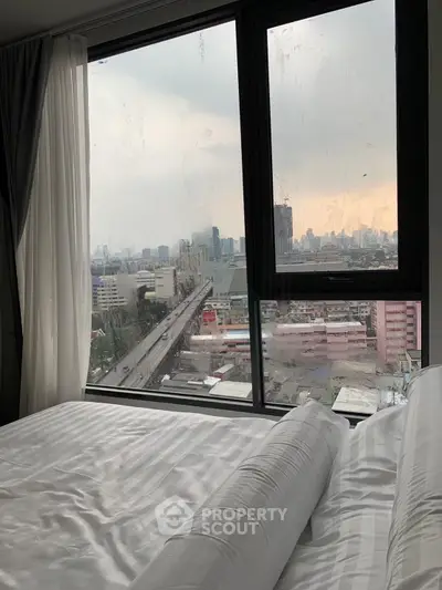 Cozy bedroom with stunning city view through large window, perfect for urban living enthusiasts.