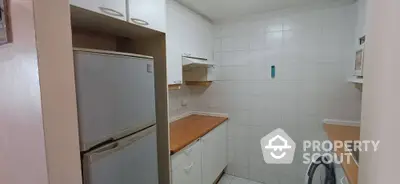 Compact kitchen with white cabinets and wooden countertops, featuring a fridge and washing machine.