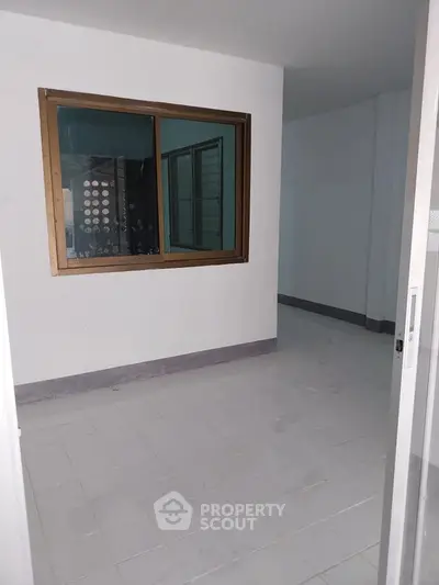 Spacious empty room with tiled floor and large window, ideal for customization.