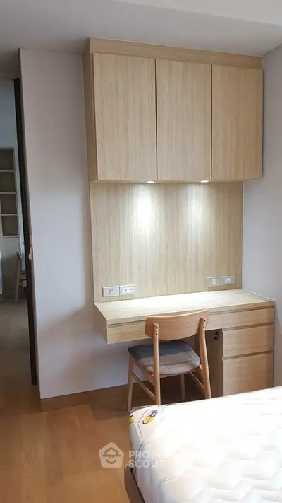 Modern bedroom with built-in wooden study desk and chair, featuring sleek cabinetry and soft lighting.