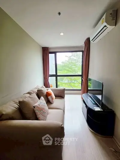 Cozy living room with large window and modern furnishings, offering a serene view of greenery.