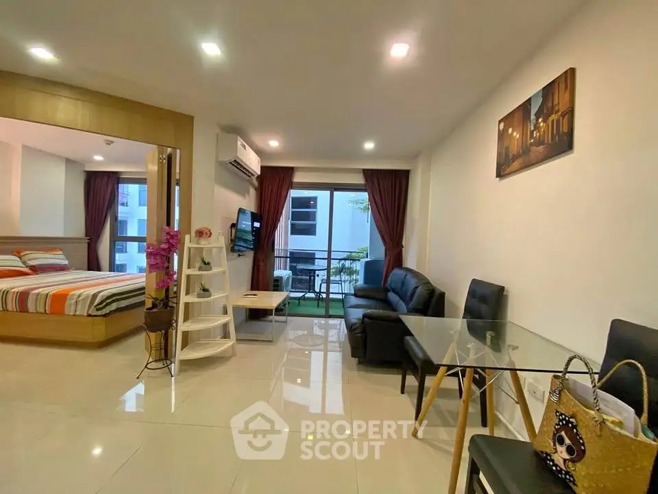 Modern open-plan living room with glass dining table and cozy seating area, leading to a spacious bedroom.