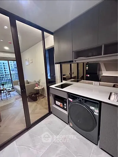 Modern kitchen with sleek appliances and view into stylish living room and balcony.