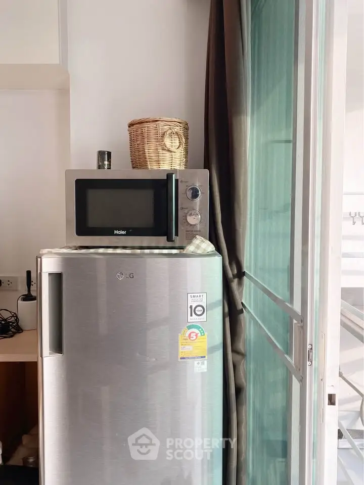 Modern kitchen corner with stainless steel fridge and microwave near window.