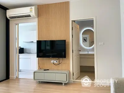 Modern living room with sleek wooden paneling, wall-mounted TV, and a glimpse of the kitchen, showcasing a blend of comfort and style.