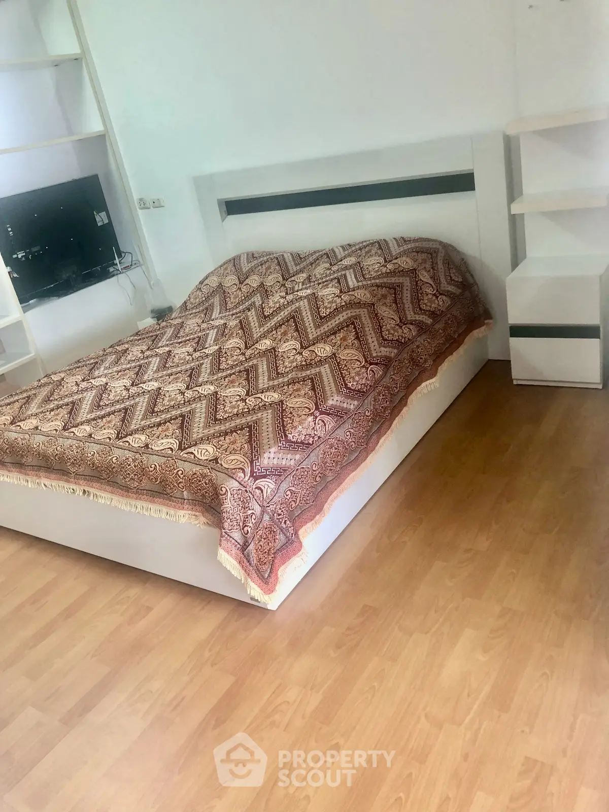 Spacious bedroom with modern design and elegant wooden flooring, featuring built-in shelves and a cozy bed.