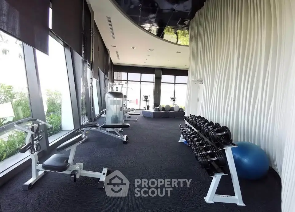 Luxurious gym with modern equipment and floor-to-ceiling windows in upscale residential building.
