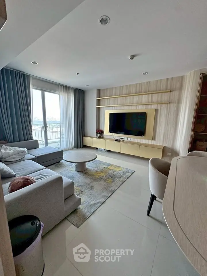 Modern living room with sleek furniture and large window offering natural light and city view.