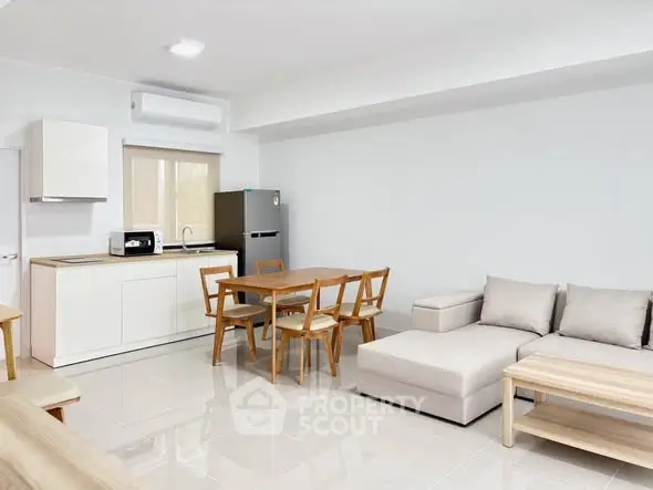 Modern open-plan living room with kitchen, featuring sleek furniture and bright natural lighting.