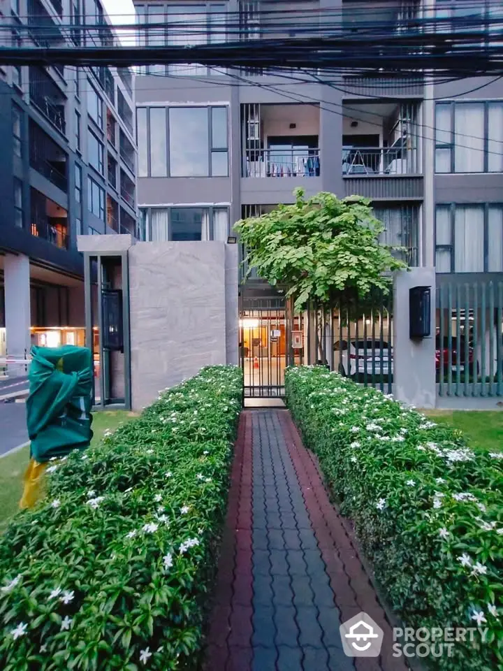 Modern apartment building entrance with lush green pathway and contemporary design.