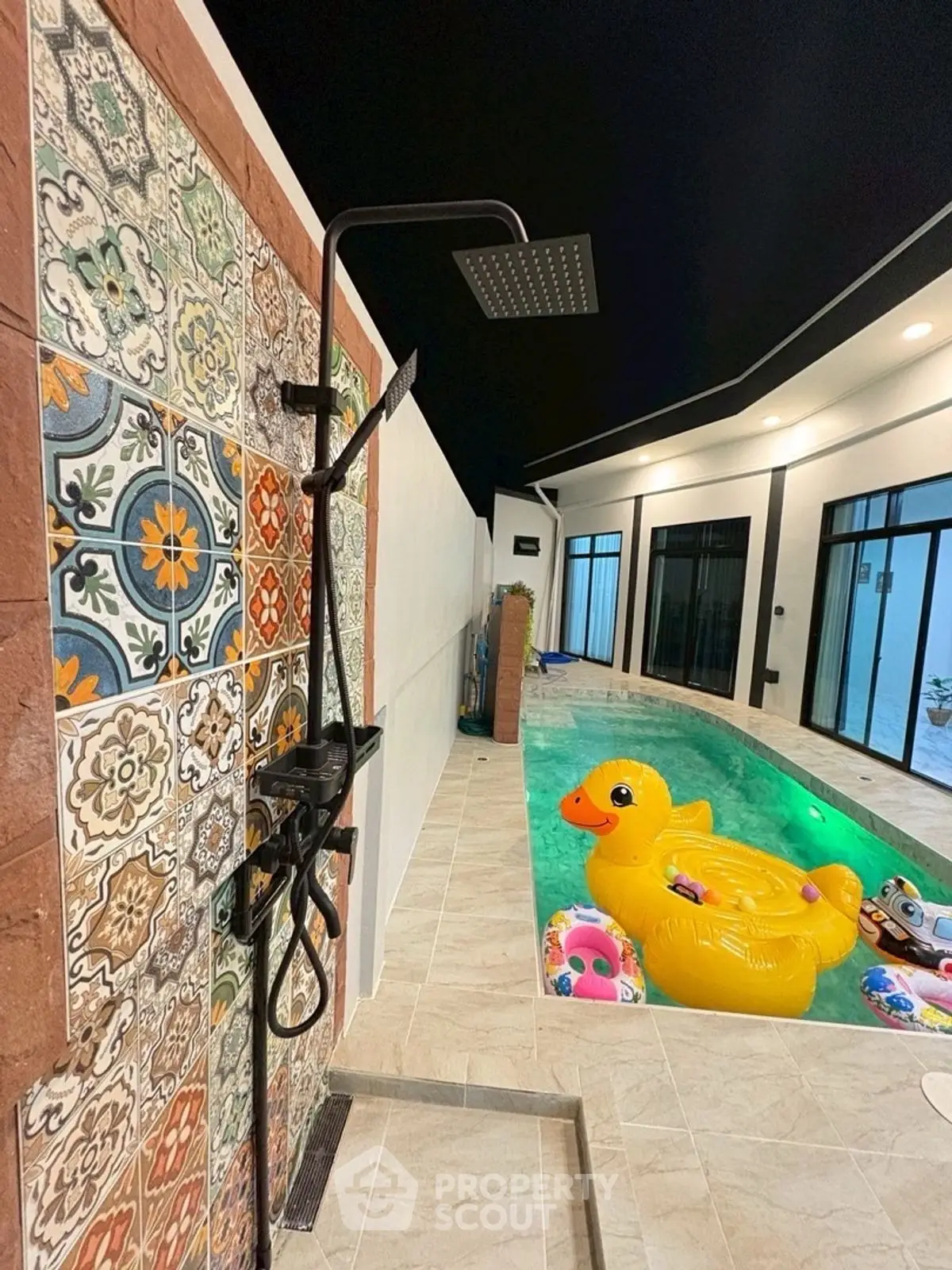 Luxurious poolside shower with vibrant tiles and inflatable duck in modern backyard