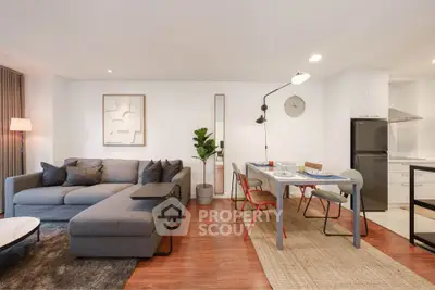 Modern living room with stylish furniture and open dining area, featuring a cozy gray sofa and sleek decor.