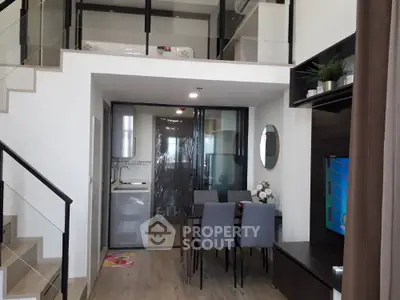 Modern duplex apartment with high ceiling living area, sleek furnishings, and a compact kitchen with stainless steel appliances.