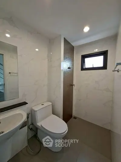 Modern bathroom with sleek fixtures and marble tiles, featuring a toilet and sink under recessed lighting.