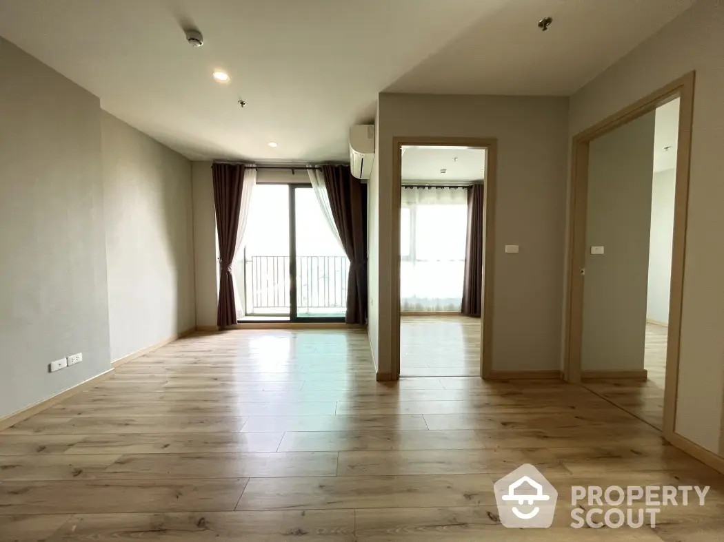 Spacious empty living room with wooden flooring and balcony access