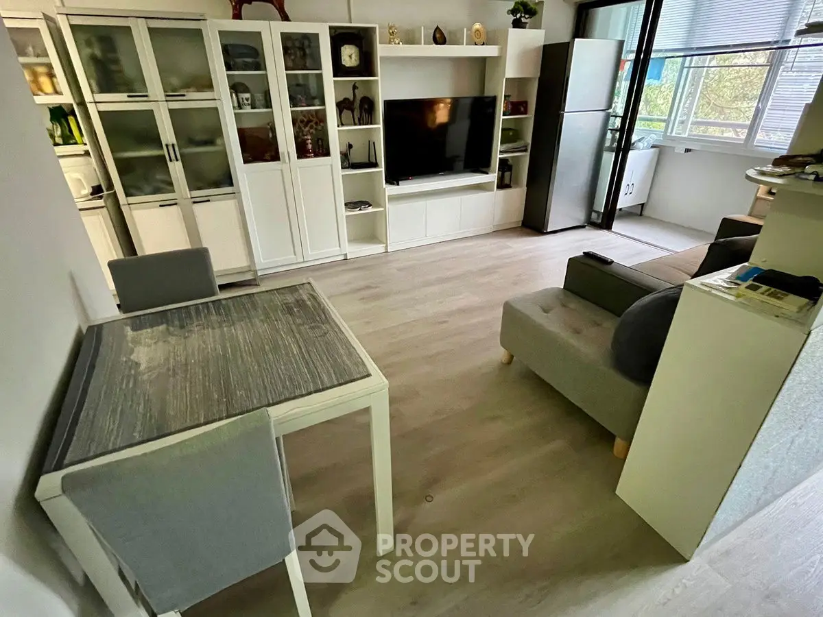 Modern living room with sleek furniture and large TV, featuring a cozy dining area and ample natural light.