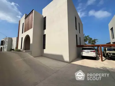 Modern minimalist building exterior with driveway and parked cars under clear blue sky.