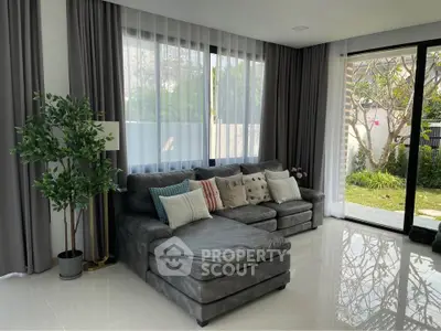 Spacious living room with modern gray sectional sofa and large windows overlooking garden.
