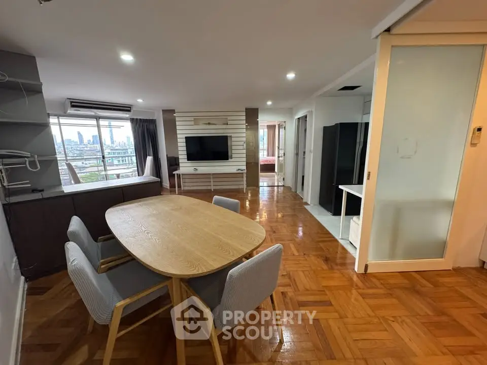 Spacious open-plan living room with dining area and city view, featuring modern furniture and wooden flooring.