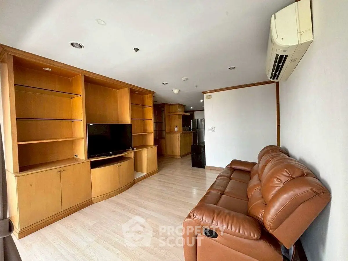 Spacious living room with leather sofa and built-in wooden shelves, perfect for relaxation.