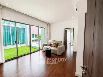 Spacious living room with hardwood floors and large windows opening to a lush green garden.