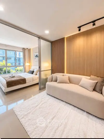 Modern living room with cozy sofa and view into stylish bedroom through sliding glass doors.