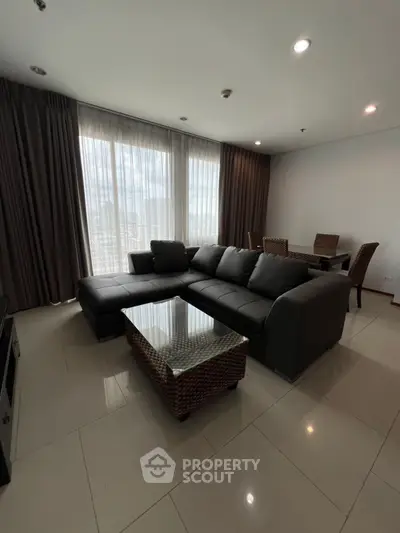 Spacious living room with modern sofa and dining area, featuring large windows and elegant decor.