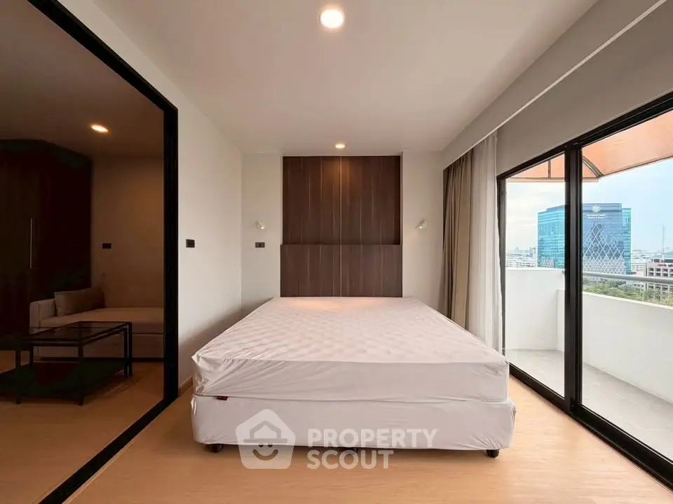 Modern bedroom with large windows and balcony offering city views, featuring a minimalist design and natural light.