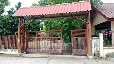 Charming rustic entrance gate with red roof and wooden fence, surrounded by lush greenery.