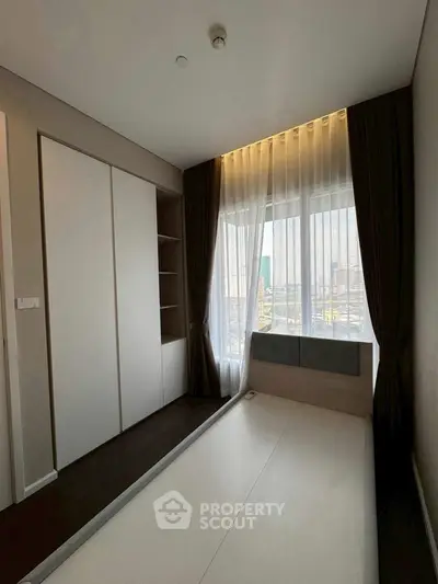 Modern bedroom with large window and built-in wardrobe, offering ample natural light.