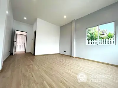 Spacious and bright empty room with wooden flooring, white walls, and a large window offering a view of greenery, ideal for a personalized living space.