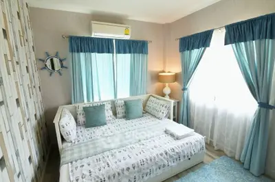 Charming bedroom with nautical decor and natural light, featuring cozy bedding and elegant curtains.