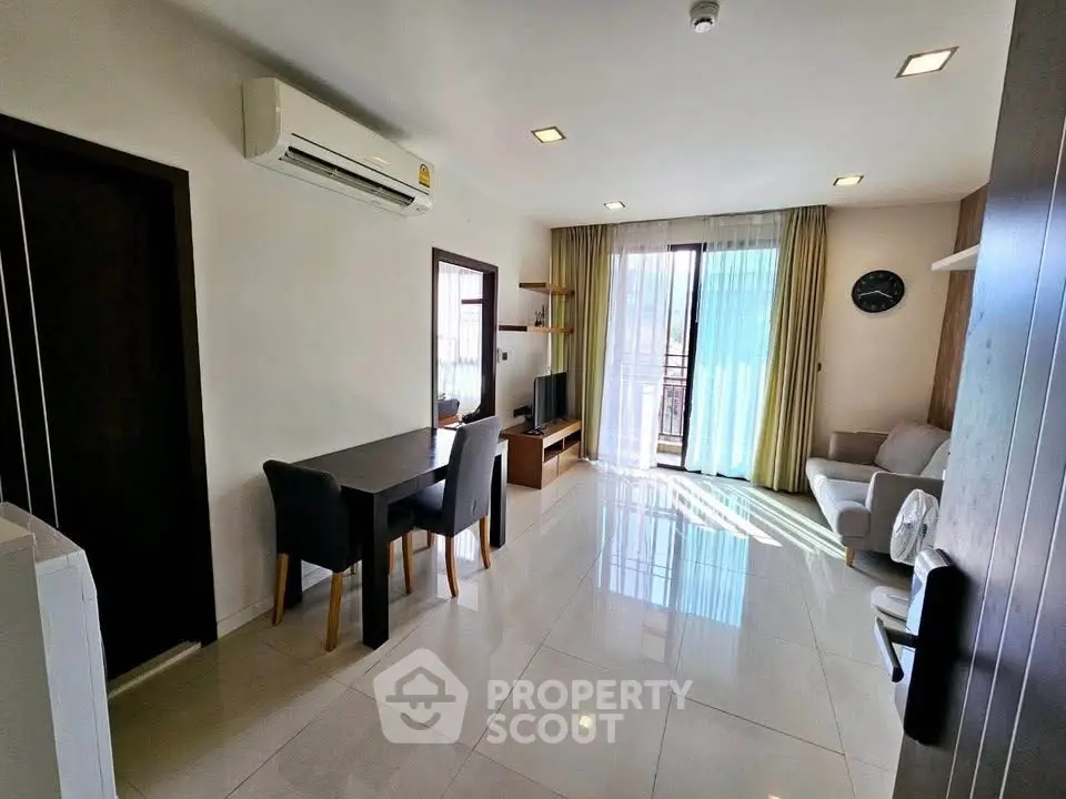 Modern living room with sleek furniture and natural light, featuring a dining area and air conditioning.