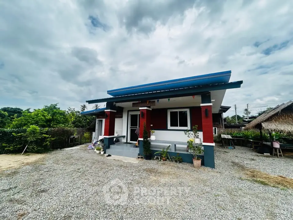 Charming single-story home with vibrant exterior and spacious gravel driveway, surrounded by lush greenery.
