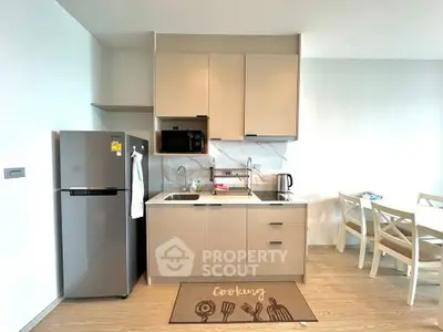 Modern kitchen with sleek cabinetry, stainless steel fridge, and dining area in a bright apartment.