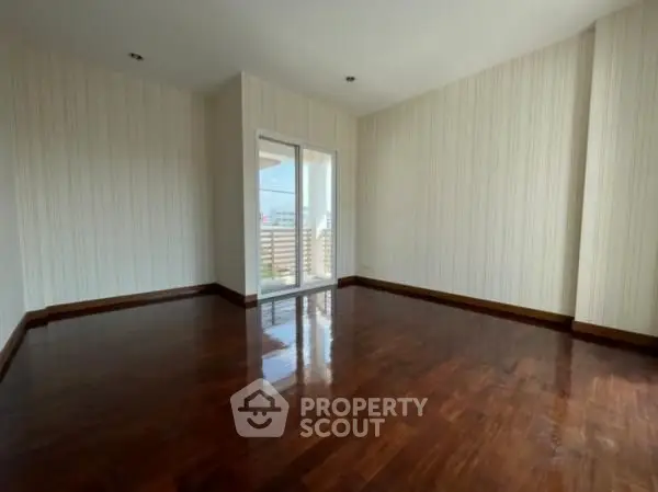 Spacious empty room with wooden floors and balcony access, perfect for customization.