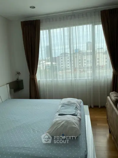 Cozy bedroom with large window and city view, featuring modern decor and natural light.