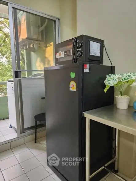 Compact kitchen area with refrigerator and microwave, adjacent to a balcony with a washing machine.