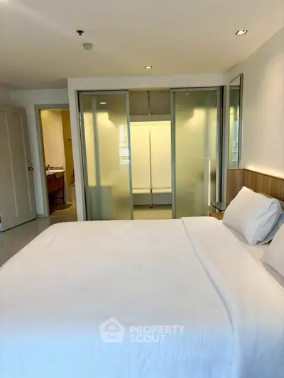 Spacious bedroom with modern design and ensuite bathroom, featuring frosted glass doors.